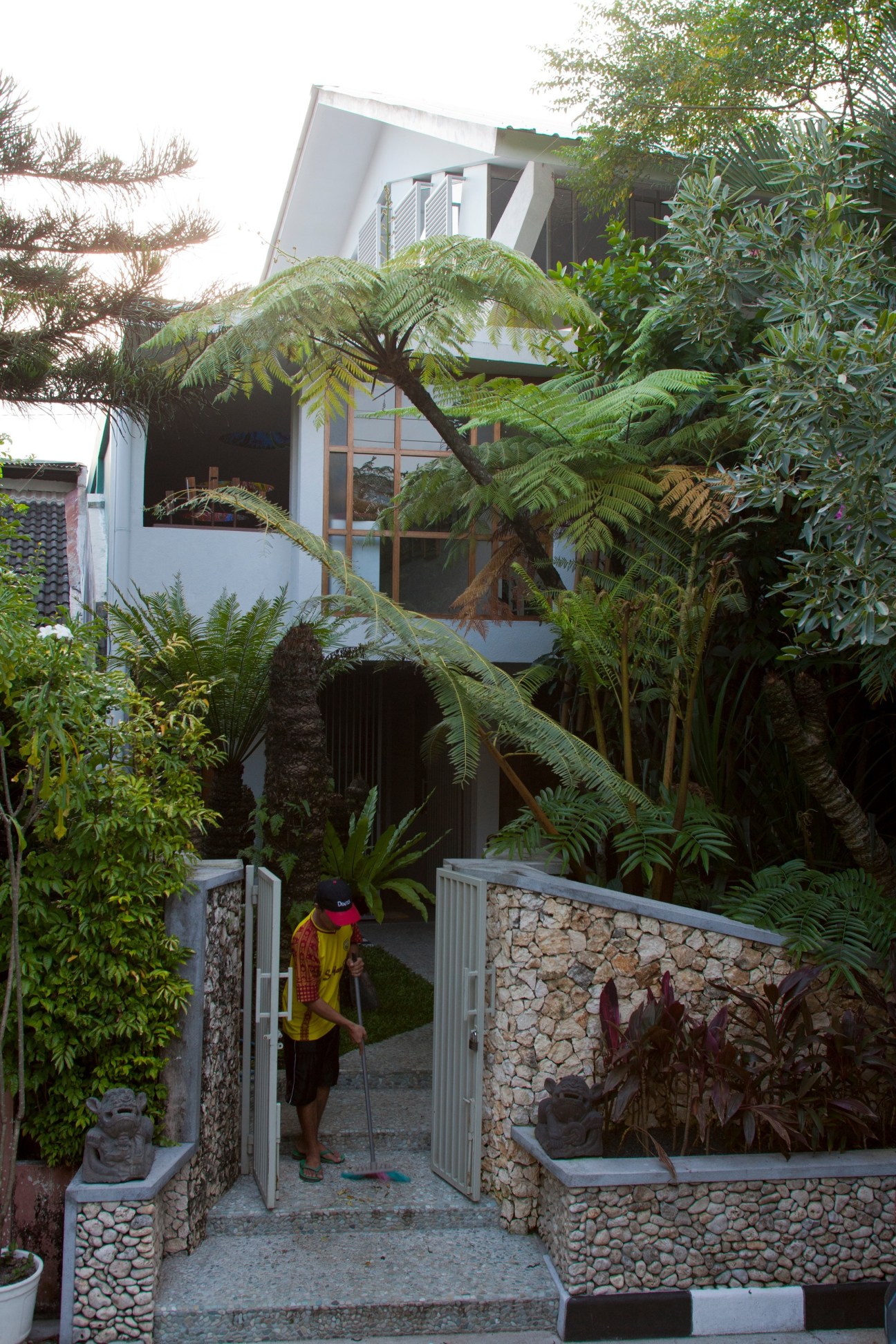 Modern white gallery building with lush tropical vegetation and stone-walled entrance designed by Eko Prawoto.