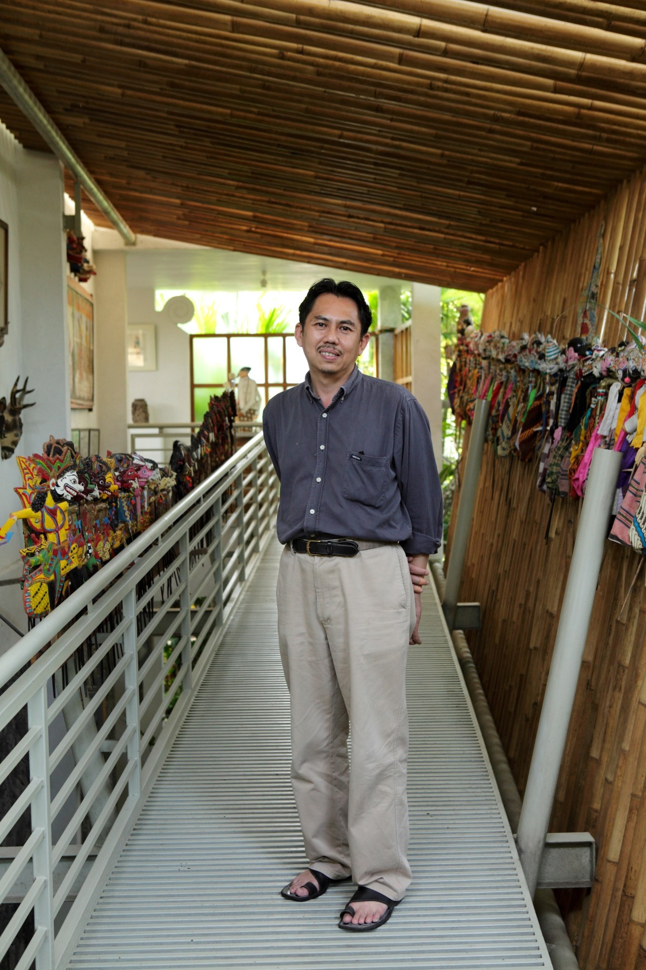 Architect Eko Prawoto stands in a wooden corridor lined with colorful batik textiles displayed on both sides.