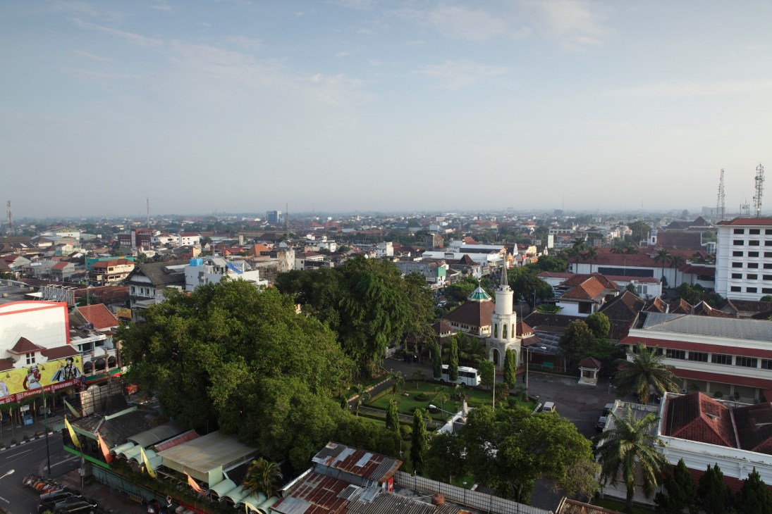 Aerial view of Yogyakarta cityscape with low-rise buildings, green spaces, and a mosque minaret.