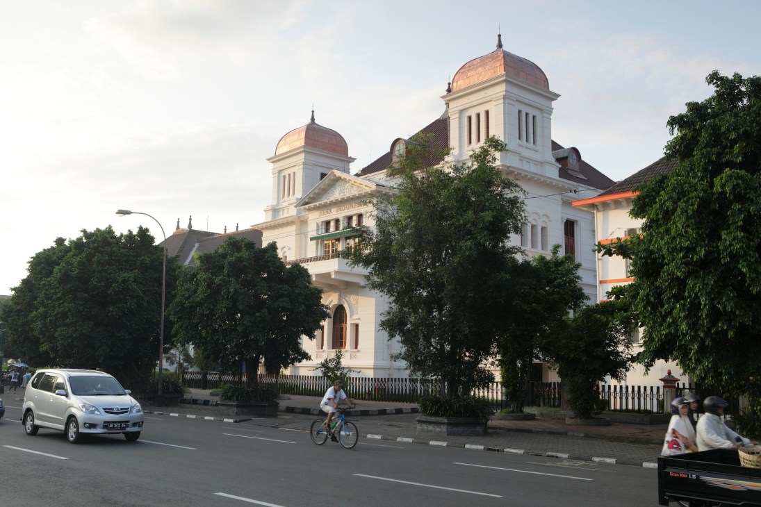 White colonial-era building with domed towers and manicured gardens fronting a street in Yogyakarta, Indonesia.