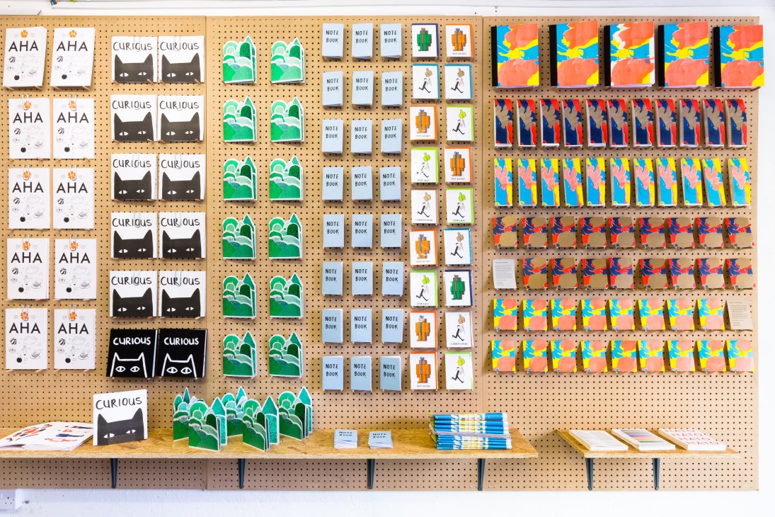 Studio Hato's London shop displays colorful printed materials, notebooks, and design products on pegboard walls.