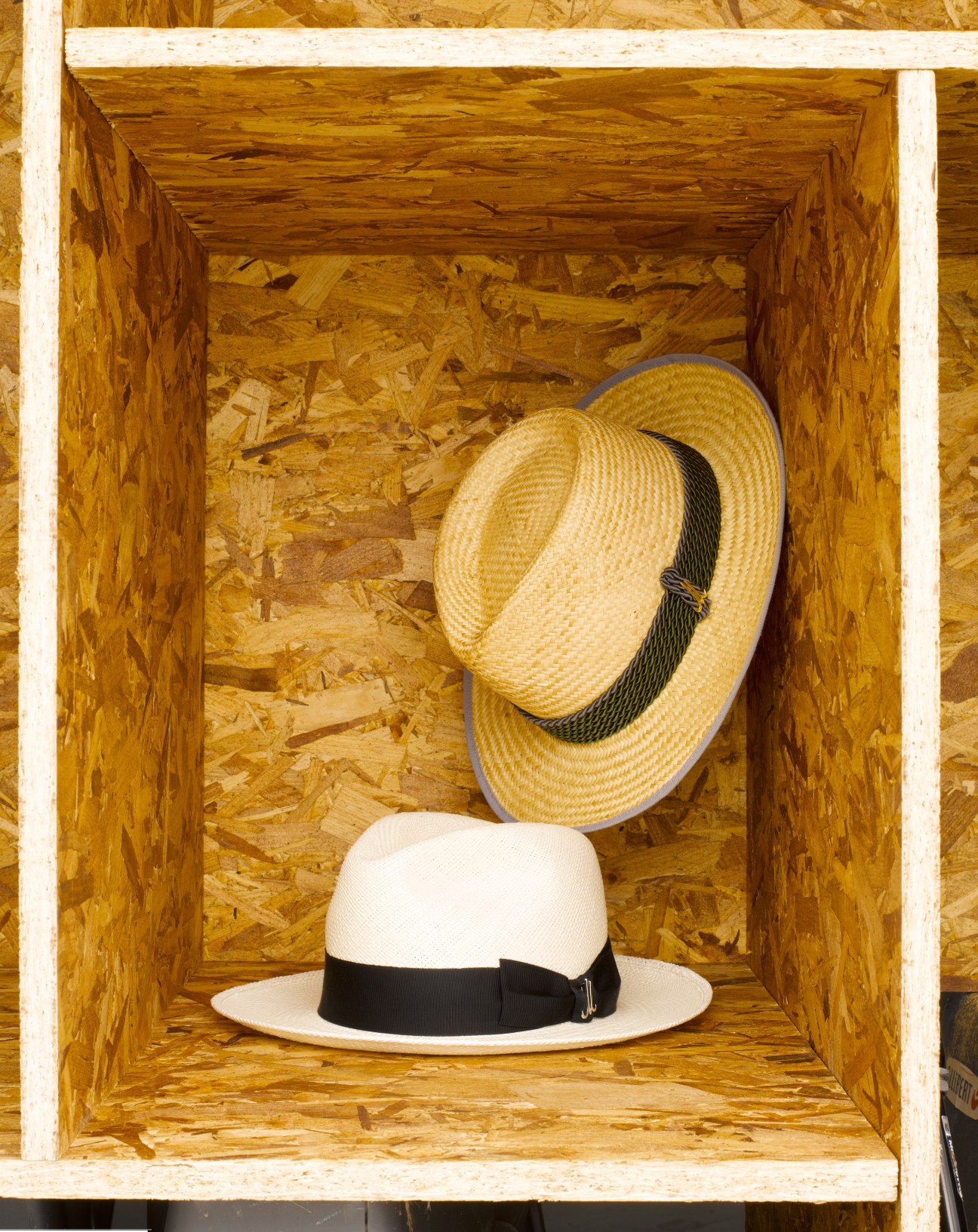 Two straw hats displayed in a wooden box: a yellow rice straw hat and a white Panama hat with black band.