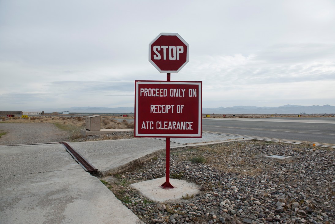 A stop sign requiring ATC clearance stands on an empty airfield with mountains visible in the background.