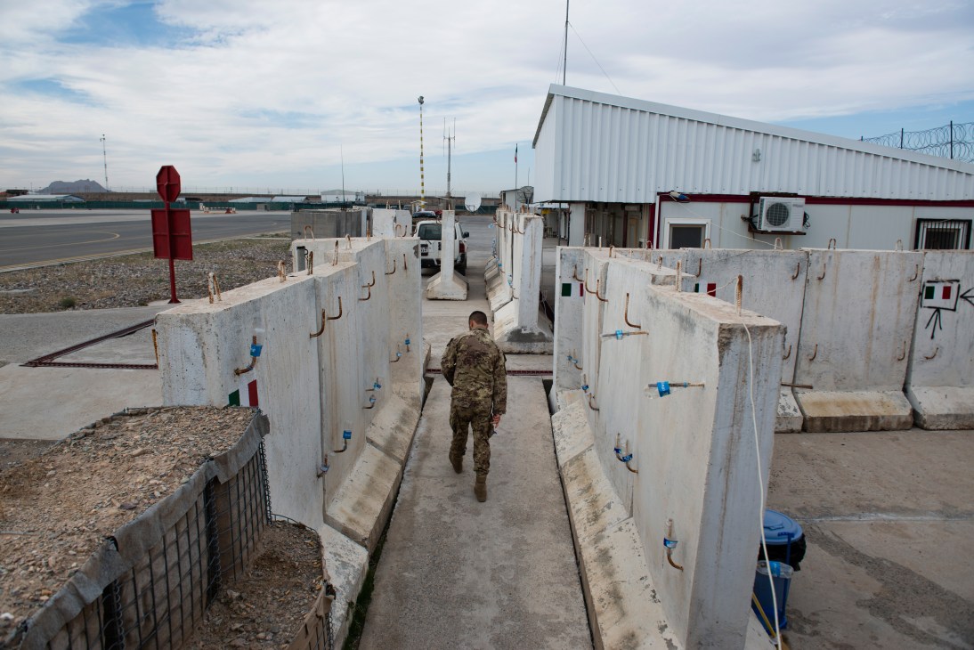 Italian soldier walking through concrete barriers at a mostly empty airfield near Herat, Afghanistan.