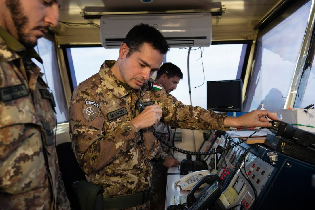 Italian Nato soldier in camouflage uniform operates air-traffic control equipment inside a military vehicle.