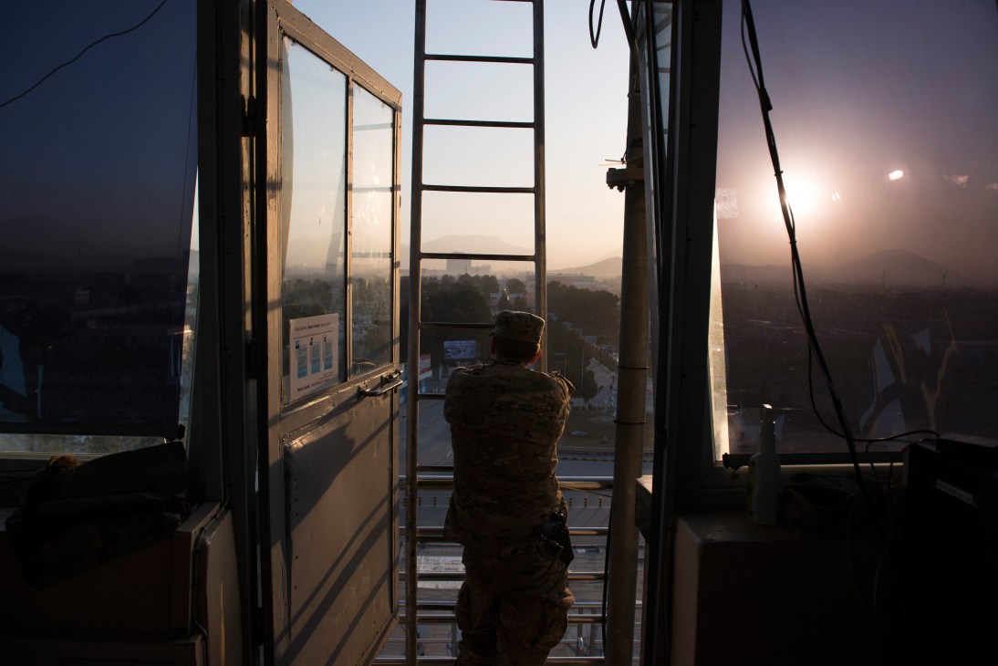 US military officer views Kabul cityscape from control tower at sunrise.