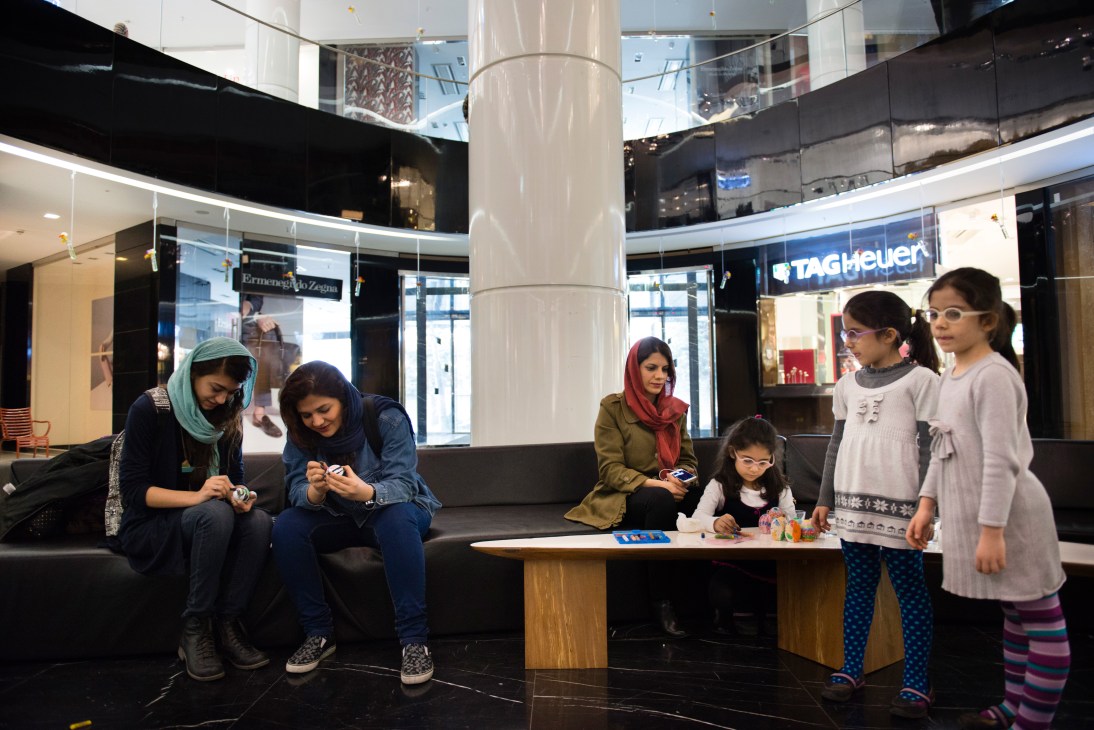 Young shoppers browsing in a Zara store at Mega Mall in Tehran, with luxury brand storefronts visible in the background.