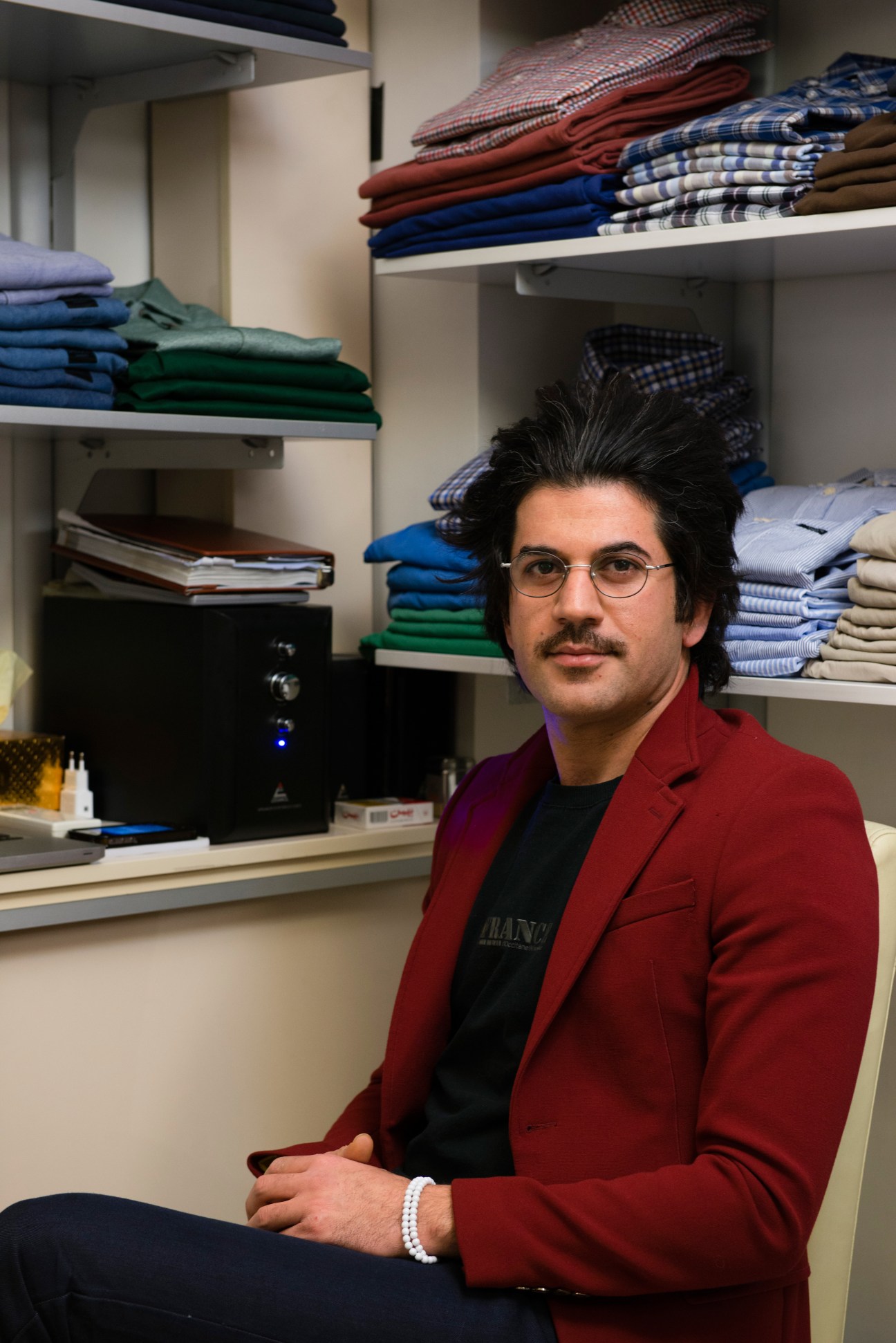 Farzad Berahman poses in his shop at Elahieh shopping centre with folded clothing stacked on shelves behind him.