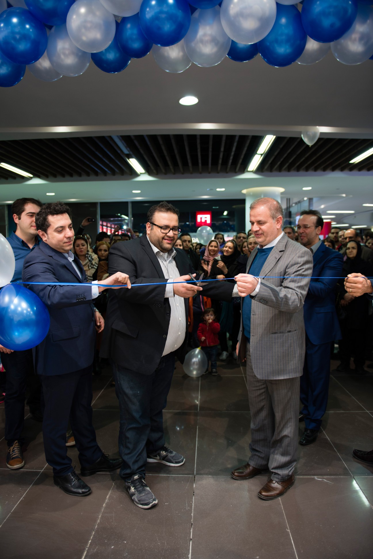 Amin Khosravi and Dr Komeili cut a ribbon at a mall opening ceremony surrounded by balloons and crowds.