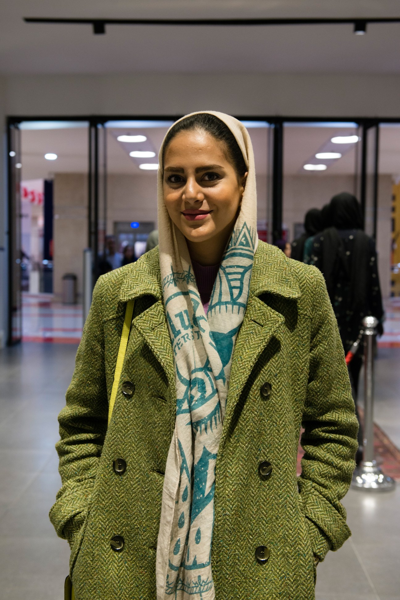 Woman in green blazer and patterned headscarf standing in modern shopping mall