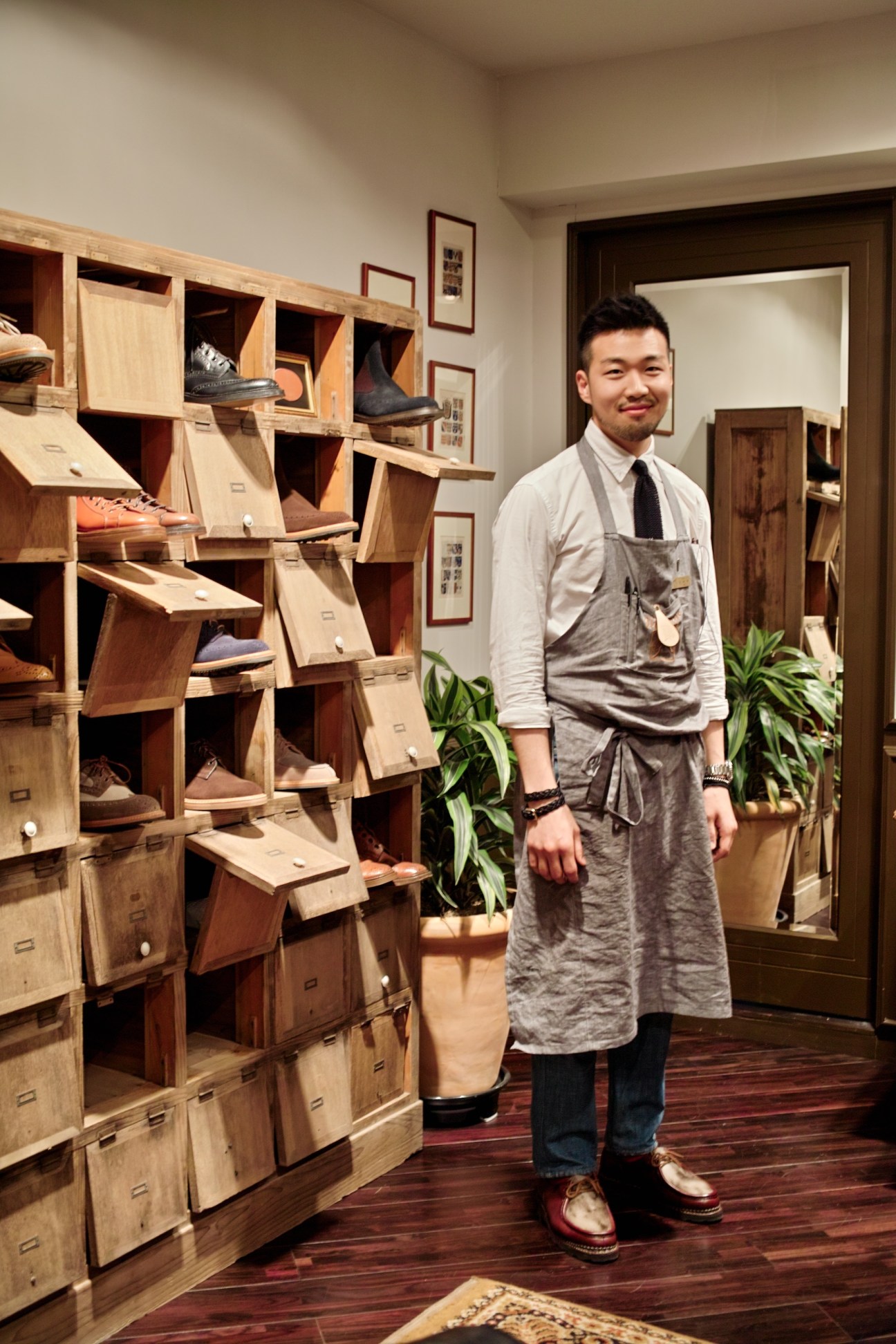 A man in an apron stands in MSK shop in Seoul, with wooden shoe shelving behind him.