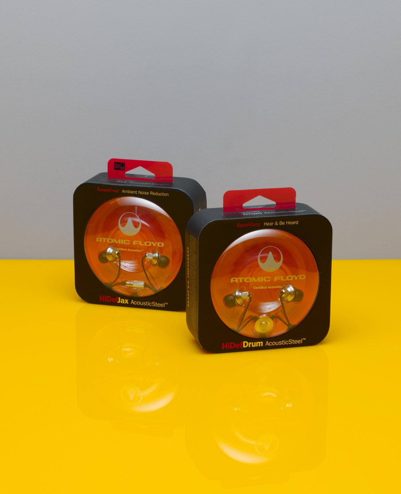Two Atomic Floyd headphone packaging boxes with orange earbud displays on yellow surface.