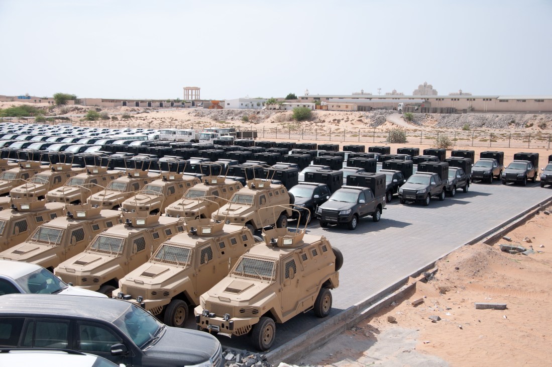 Armoured vehicles lined up in rows at an industrial facility in a desert landscape.