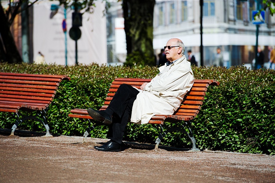 Elderly man in light coat and glasses sitting on red bench in Helsinki park