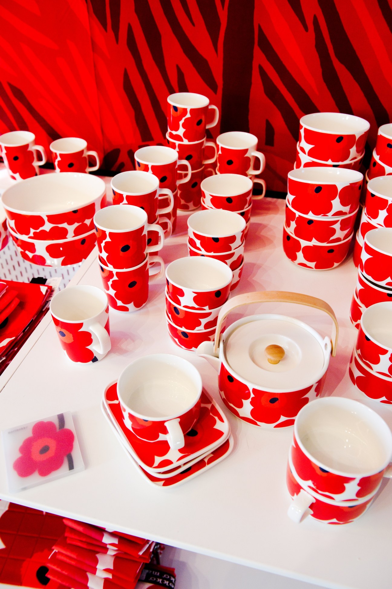 Red and white Marimekko poppy-patterned tableware displayed on a white surface with red fabric backdrop.