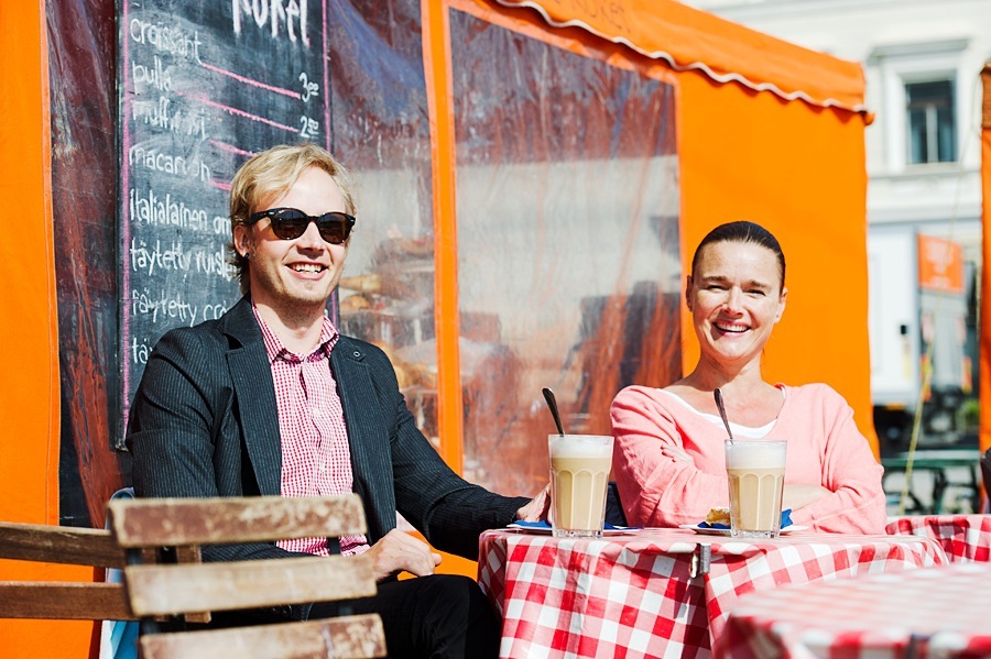 Two people dining at an outdoor café with bright orange awning in Helsinki.