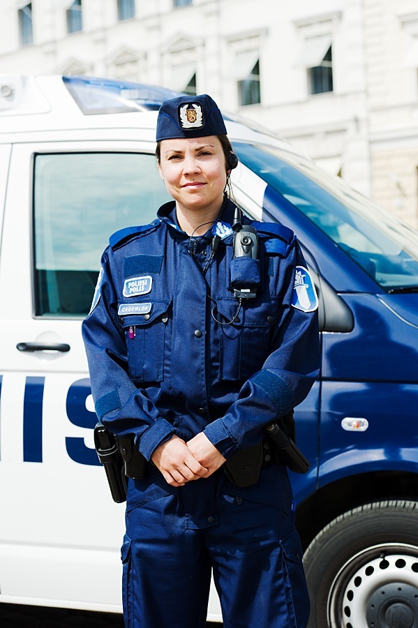 Female Finnish police officer in blue uniform standing in front of a police van.