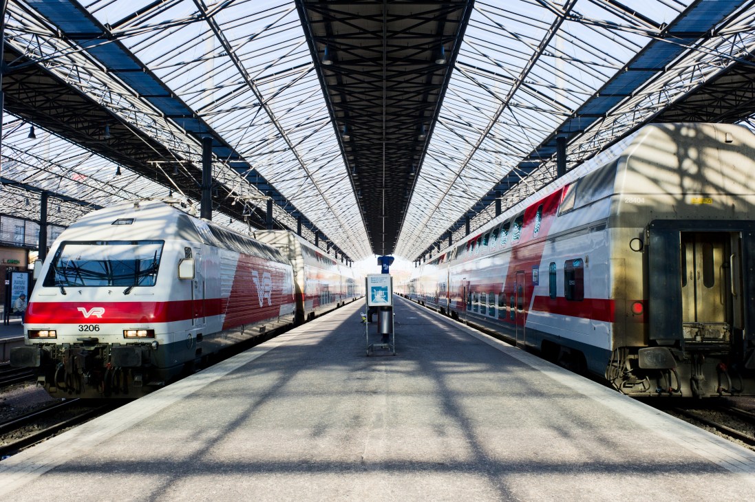 Two red and white trains at a platform under a glass and steel station roof.