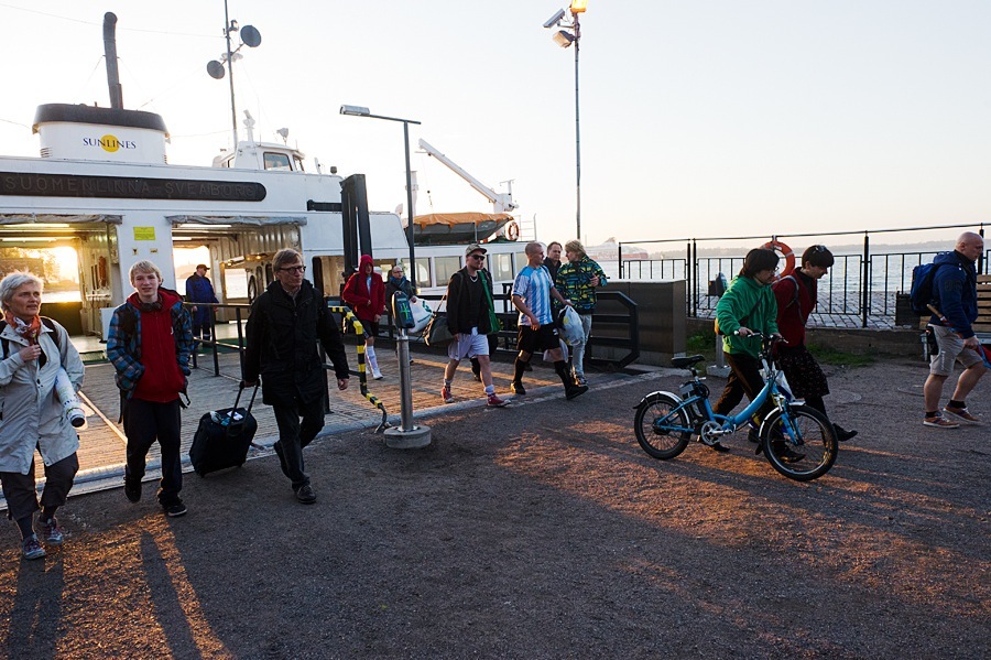 People walking and cycling near a ferry terminal at dusk in Helsinki.