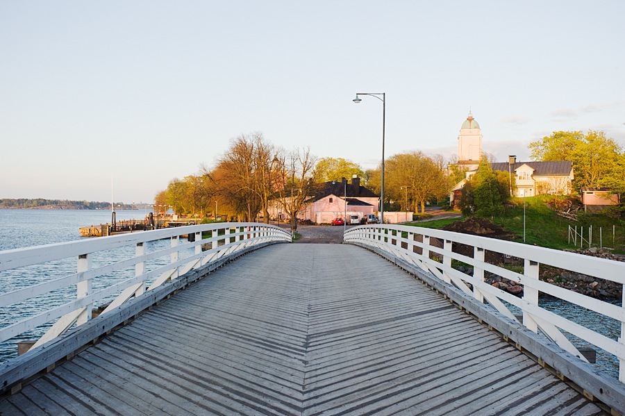 White wooden pier extending into calm water with trees and buildings visible on the shoreline.
