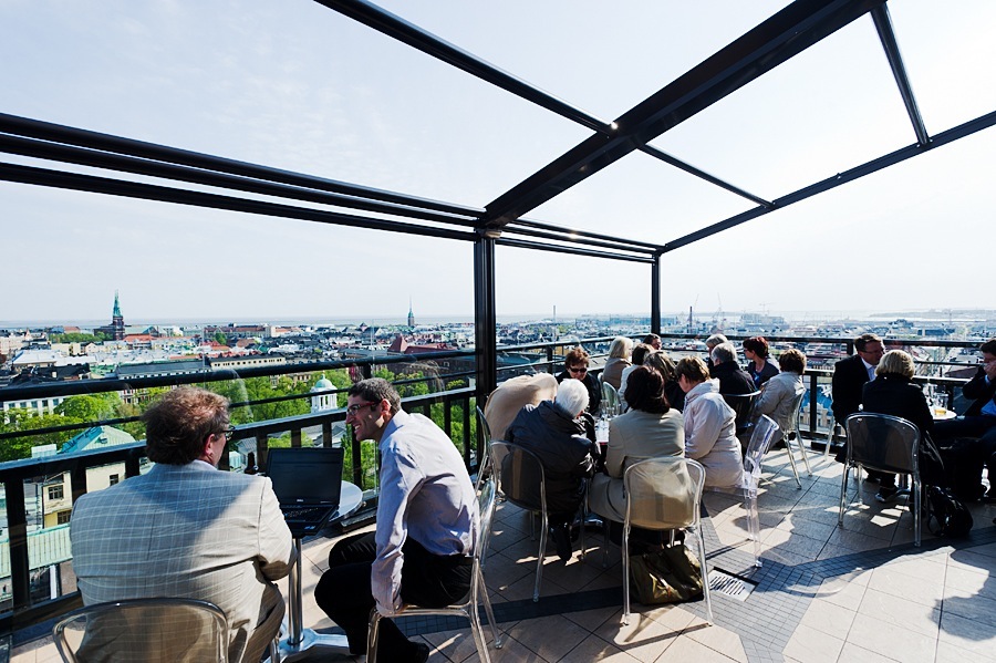 People gathered on a rooftop terrace with cityscape views under a modern black pergola structure.