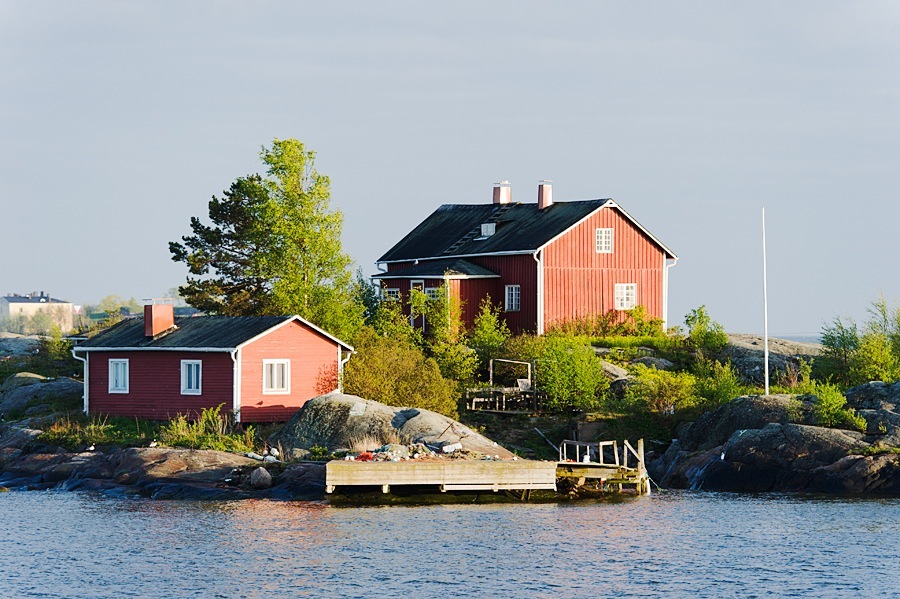 Red and orange wooden houses on a rocky island with a wooden dock in Helsinki's archipelago.