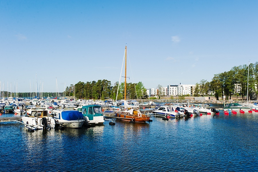 Helsinki waterfront with moored sailboats and residential buildings in background under clear sky.