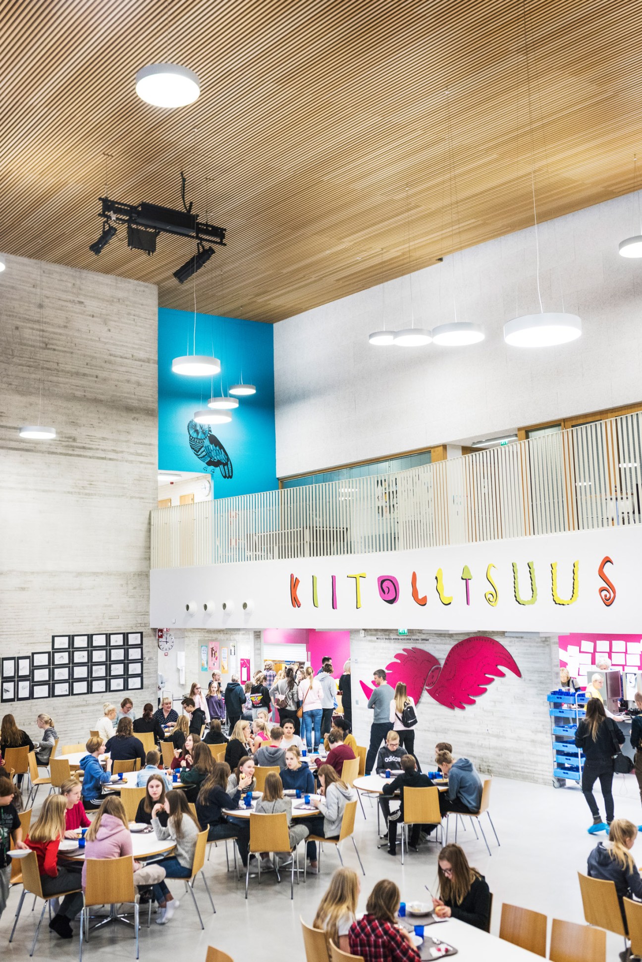 Bright interior of Saunalahti school dining hall with children seated at tables, colorful signage, and wooden ceiling.