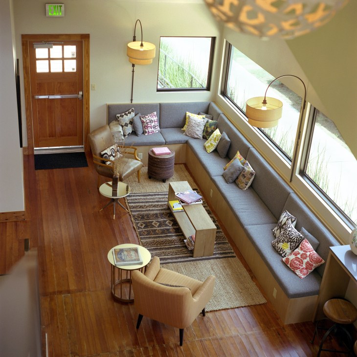 Bright foyer of Heywood Hotel with wooden flooring, gray seating, and large windows overlooking greenery.