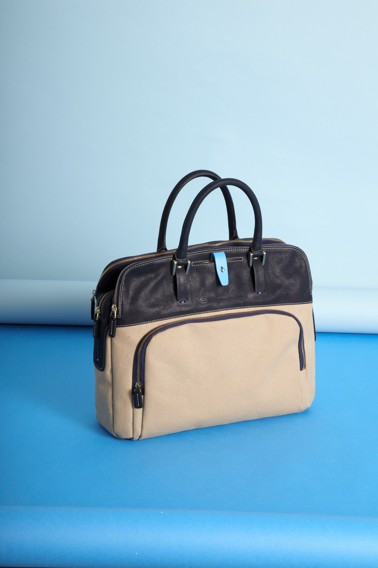 Piquadro leather and canvas city bag in black and cream with dual handles and blue tag.