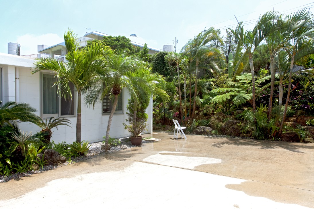 White modernist house with terrace surrounded by lush tropical plants and palm trees in Okinawa.