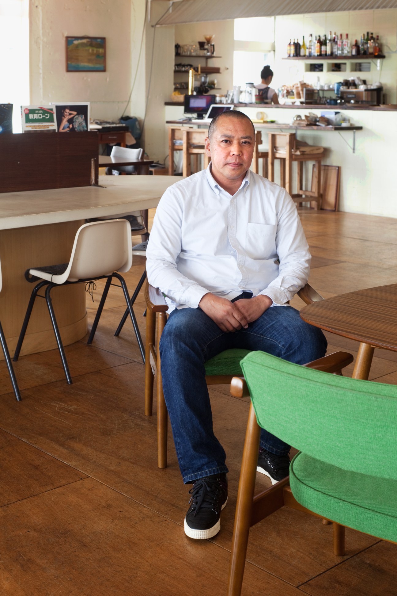 Yasushi Higa, architect, sitting in a minimalist interior space with wooden furniture and white walls.