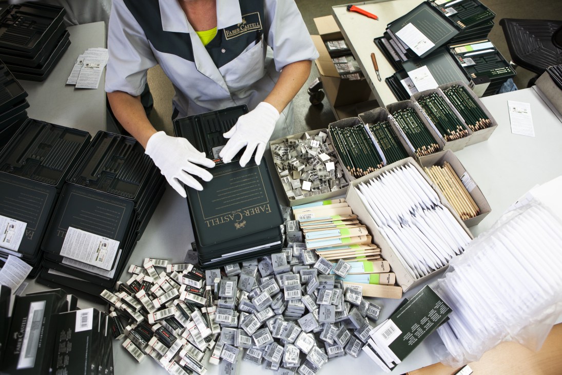 Worker in white gloves packing Faber-Castell pencils into boxes at a production facility.