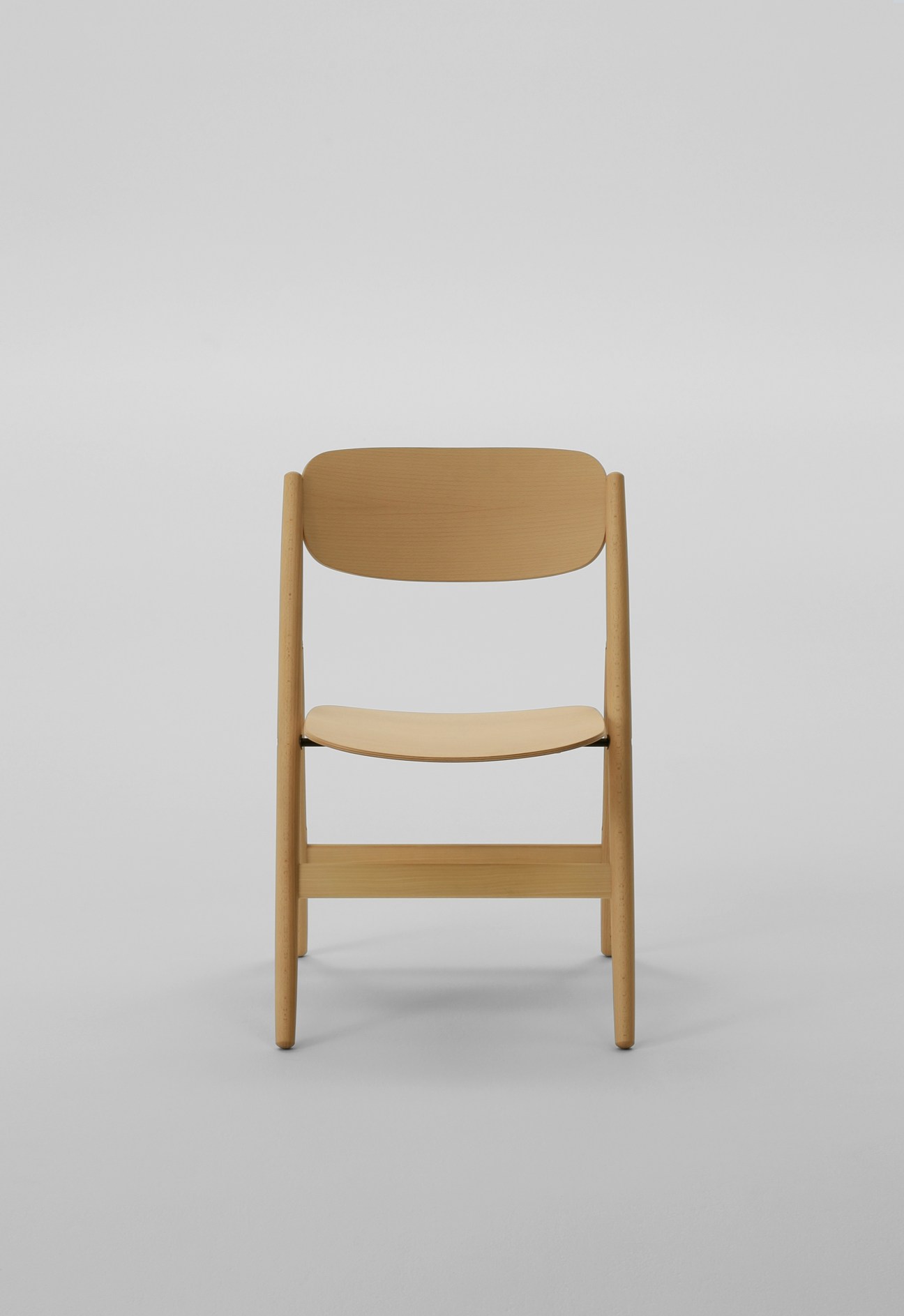 Wooden folding chair with natural beech finish, rounded backrest and seat, designed by Naoto Fukasawa for Maruni Wood Industry.