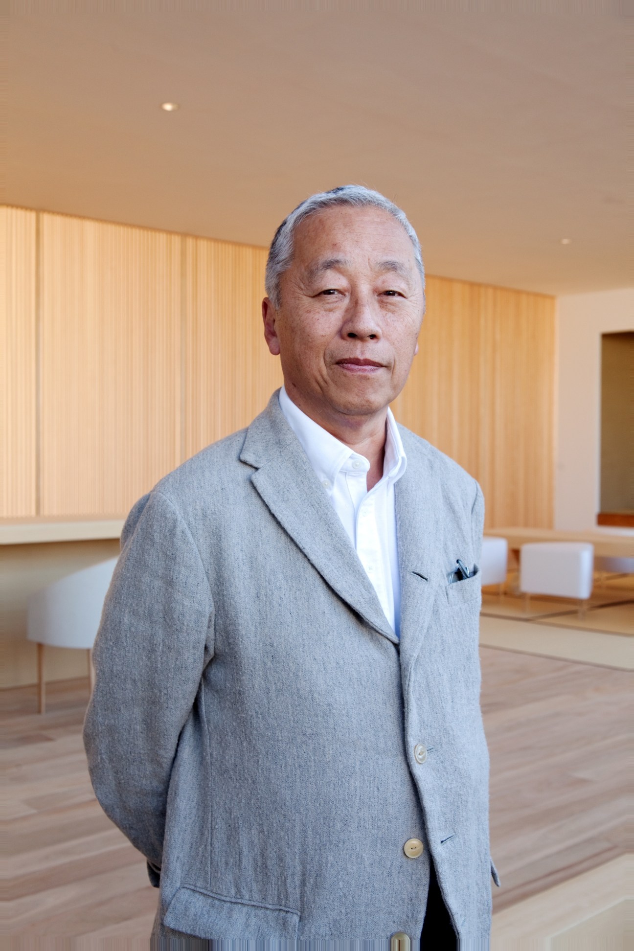 Hiroshi Sugimoto, photographer and artist, standing in a minimalist interior with wooden flooring and light wood paneling.