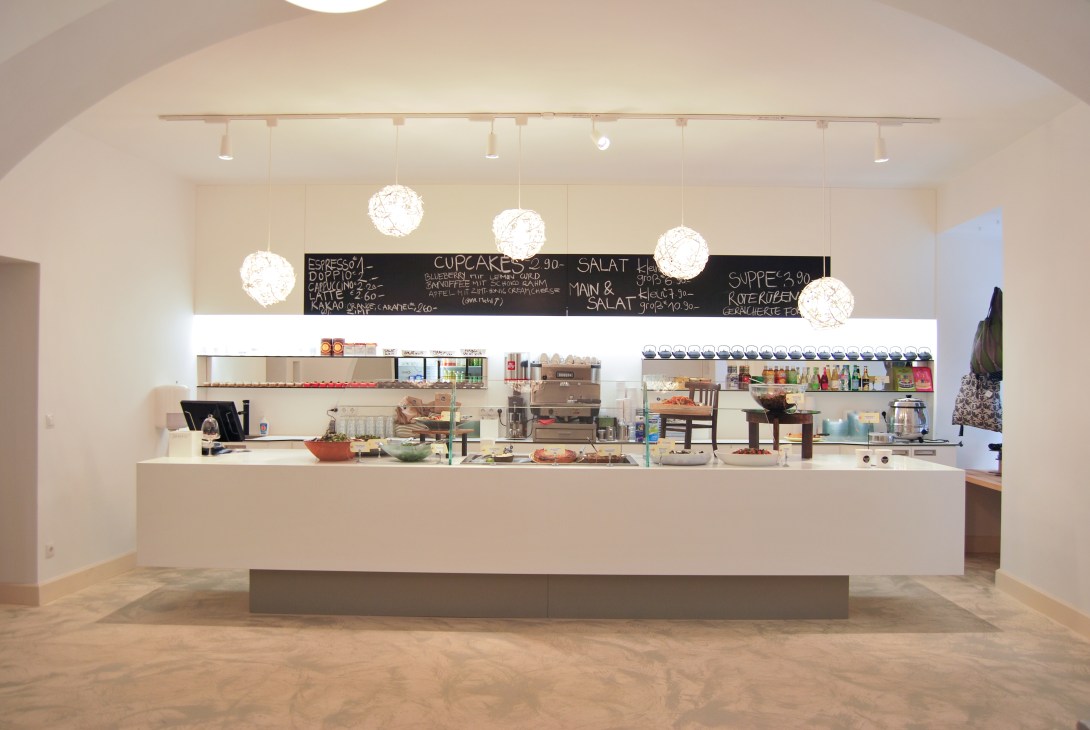 Interior of Hidden Kitchen cafe showing minimalist white counter with hanging pendant lights and menu board.