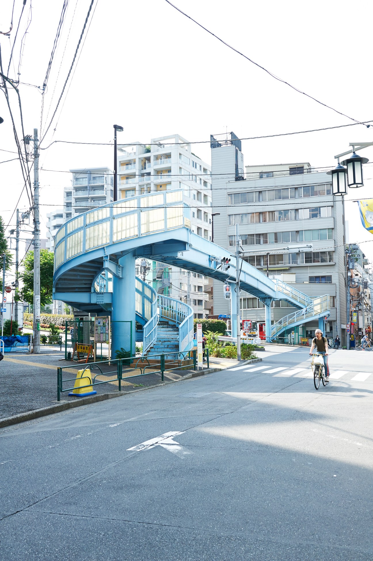 Blue pedestrian flyover with curved ramps and staircase in Tokyo street with buildings and cyclist.