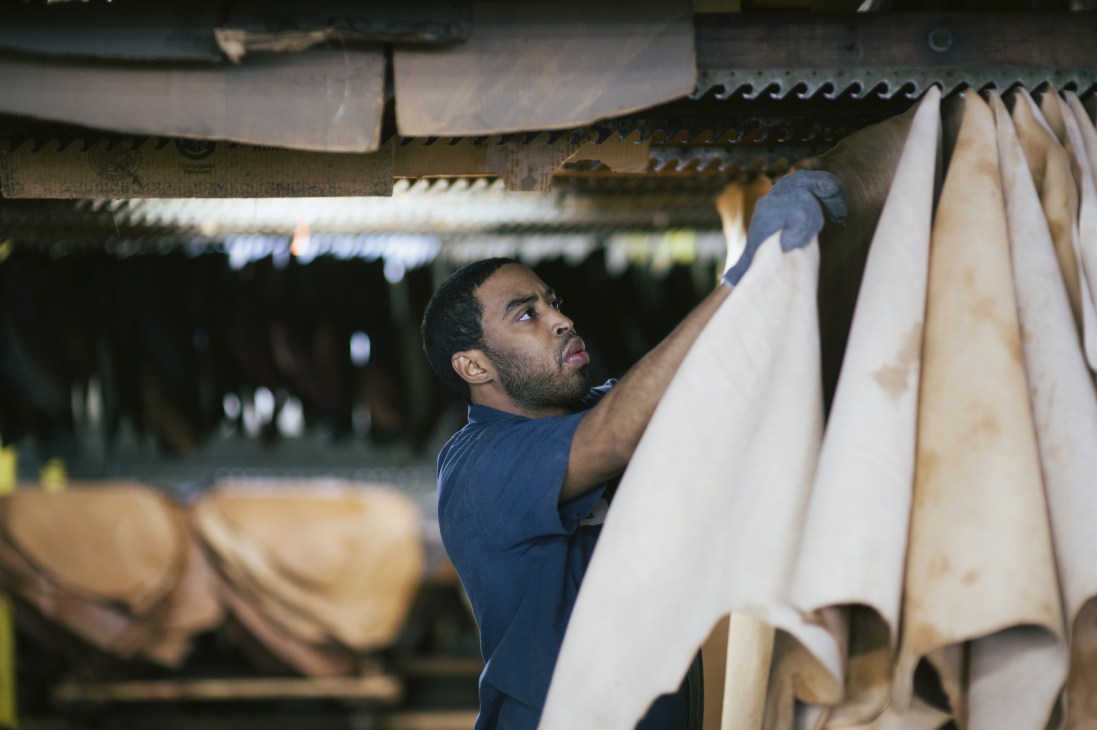 Worker hanging cream-colored leather hides in an industrial tannery facility.