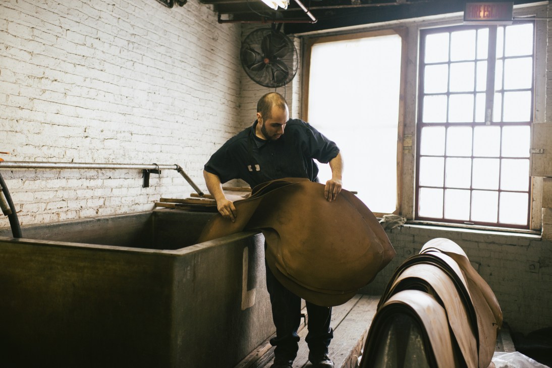 Worker handling large piece of brown leather over industrial vat at Horween Leather tannery.