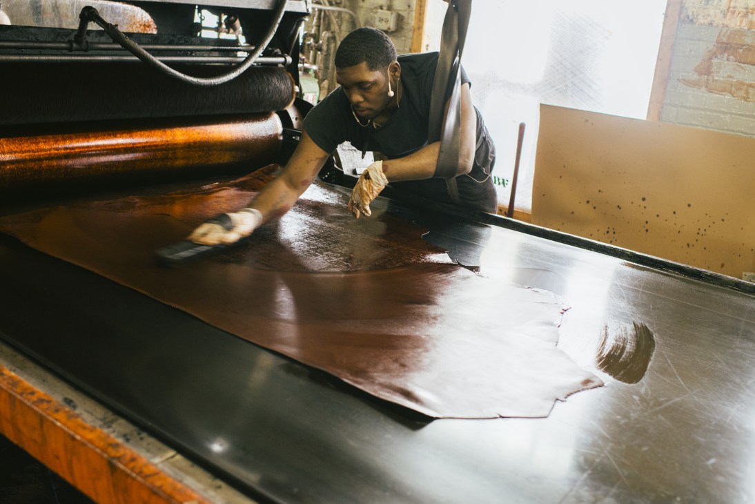 Worker at Horween Leather Company preparing brown leather hide on a work surface.