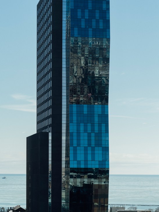 Modern skyscraper with blue glass facade and reflective windows overlooking waterfront.