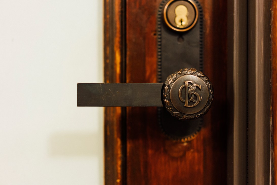 Ornate brass door handle with monogram on wooden door in the Old Colony Building.