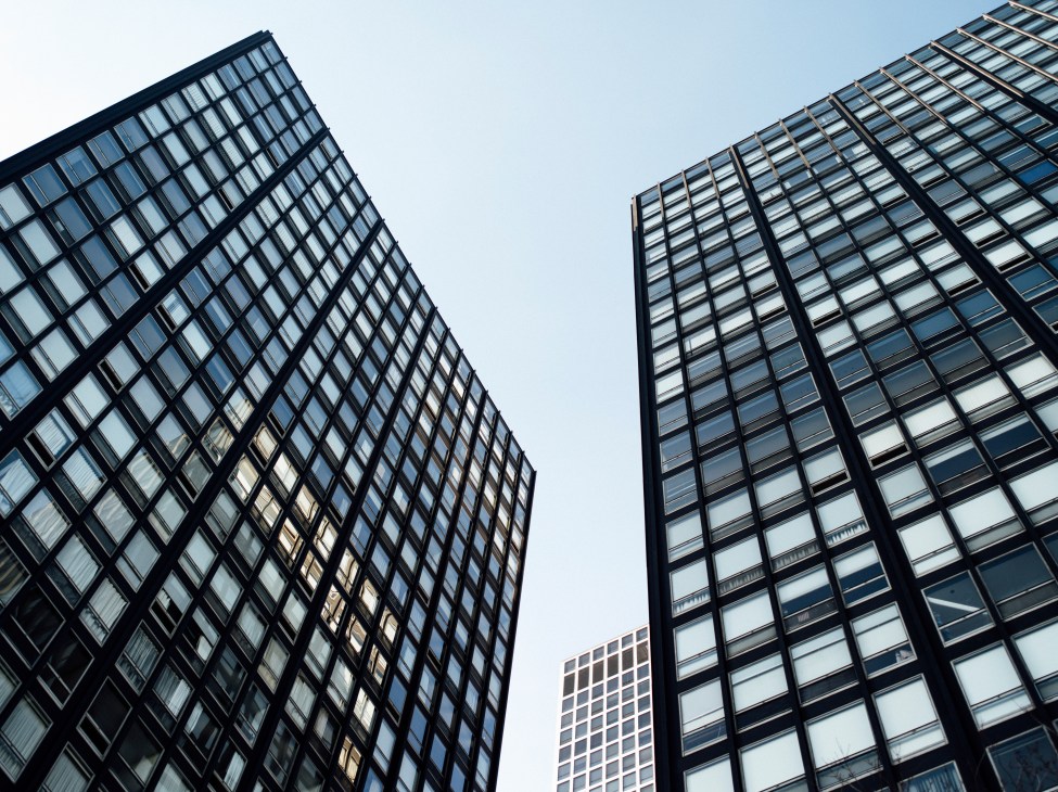 Two modernist glass and steel skyscrapers with gridded window patterns designed by Mies van der Rohe, photographed from below against a clear sky.