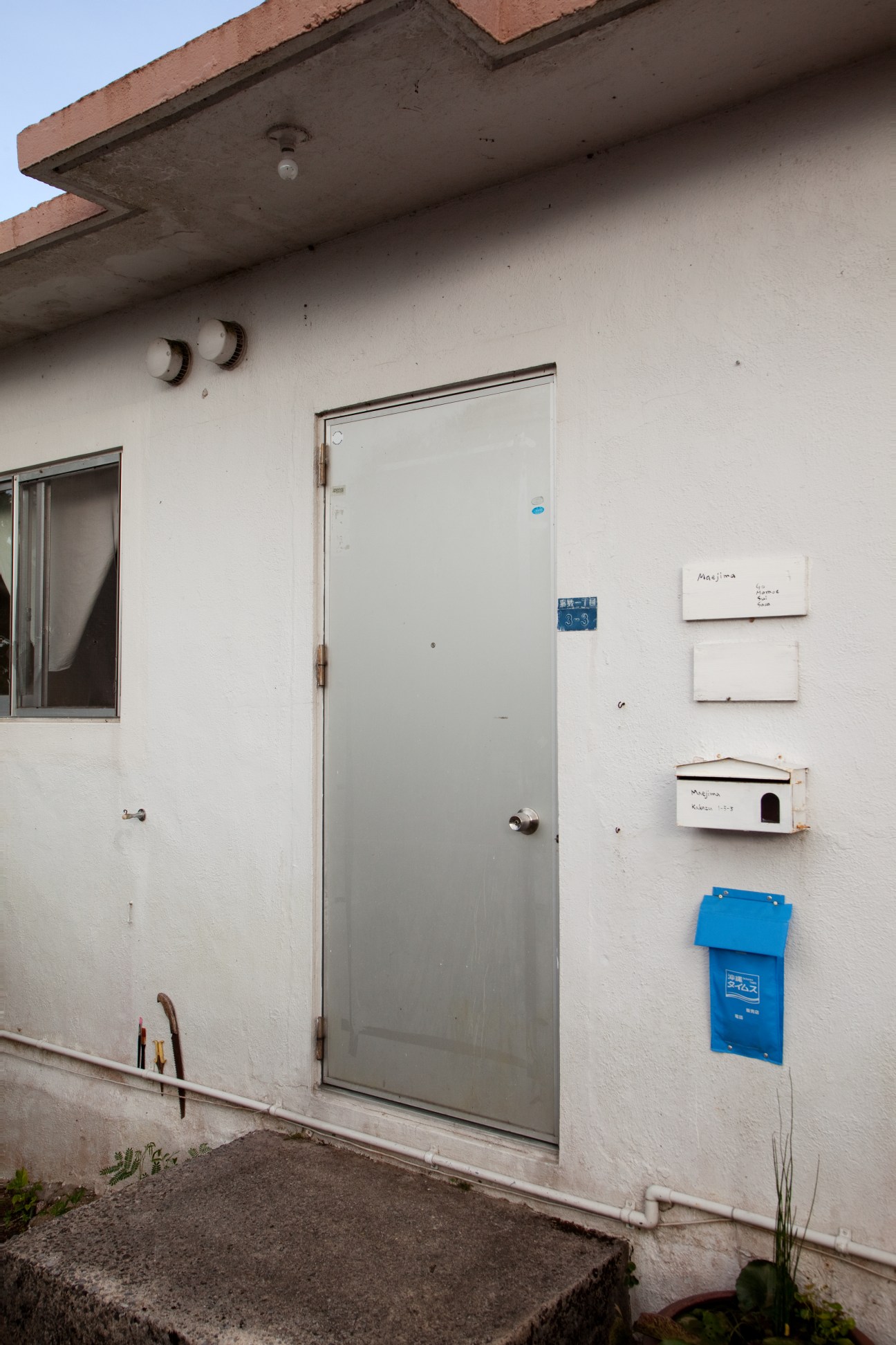 White concrete wall with metal door and mailbox entrance to a post-war military house.