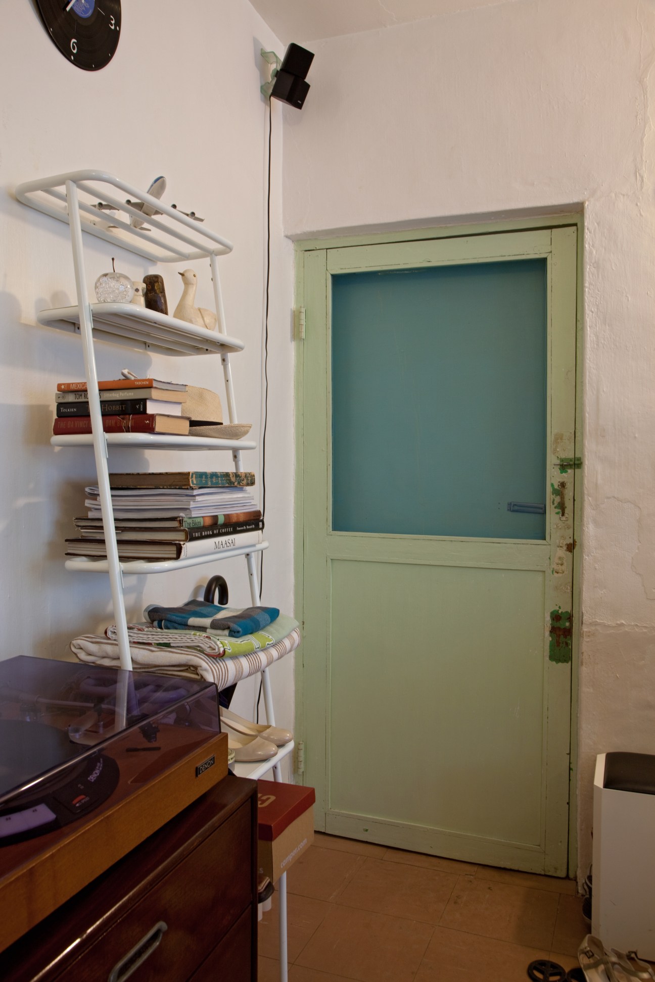 Interior entryway with vintage green wooden door, white shelving unit with books, and wooden furniture.