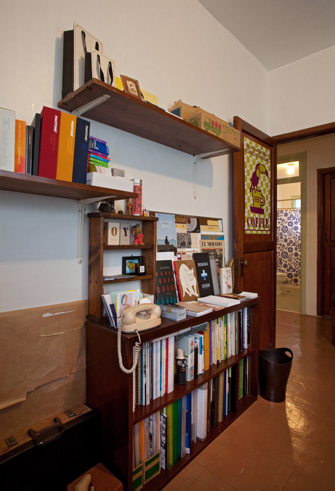 Interior of a work room featuring wooden shelving units filled with colorful books, design materials, and decorative objects.