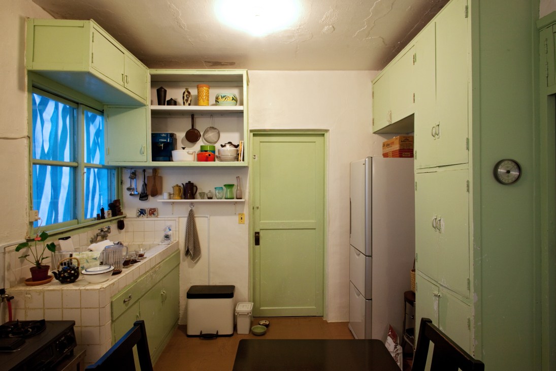 Vintage kitchen with mint-green cabinetry, open shelving, and period fixtures in a post-war military house.