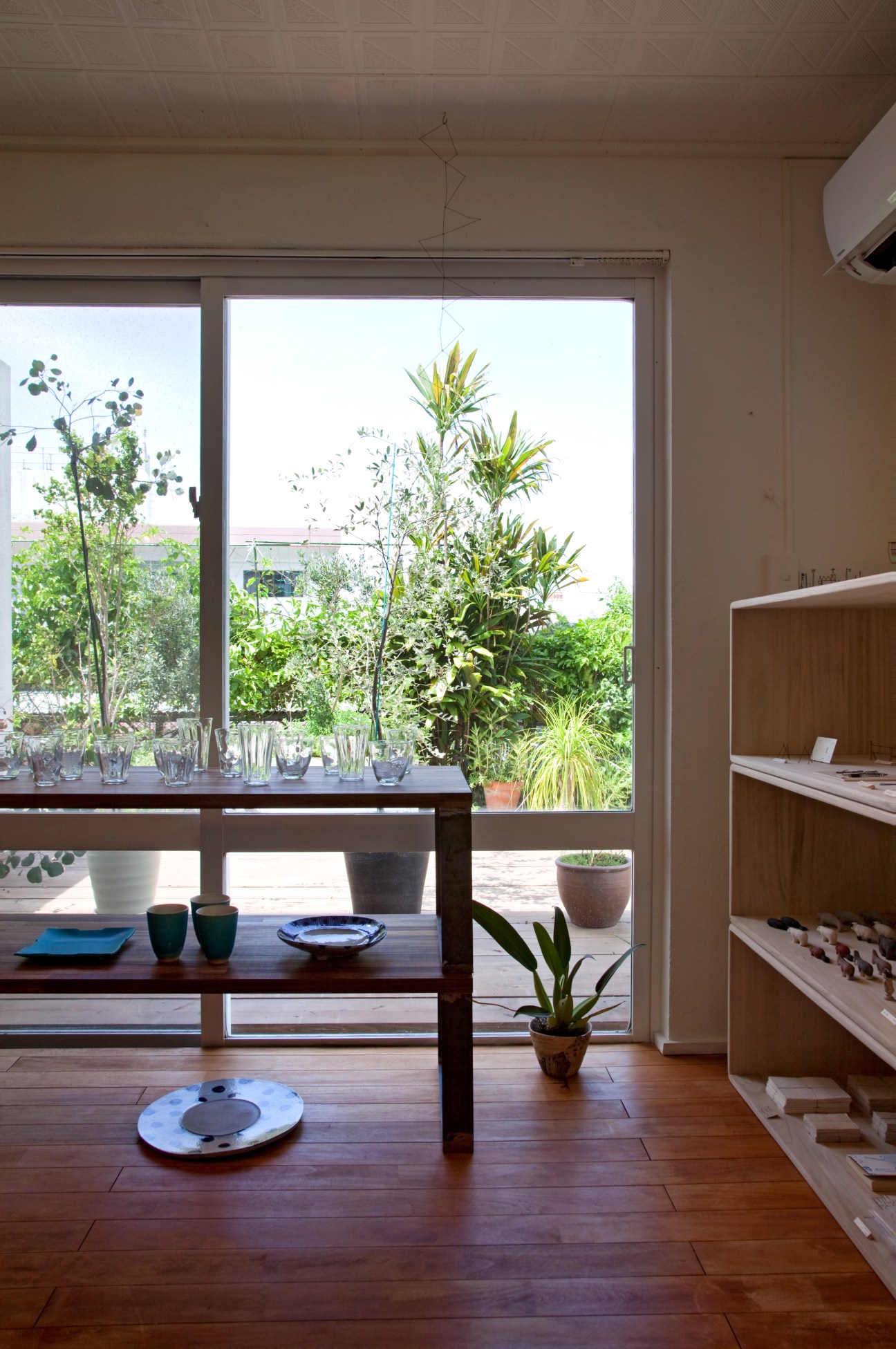 Interior of Ten shop with wooden table, potted plants on windowsill and garden view through large glass doors.