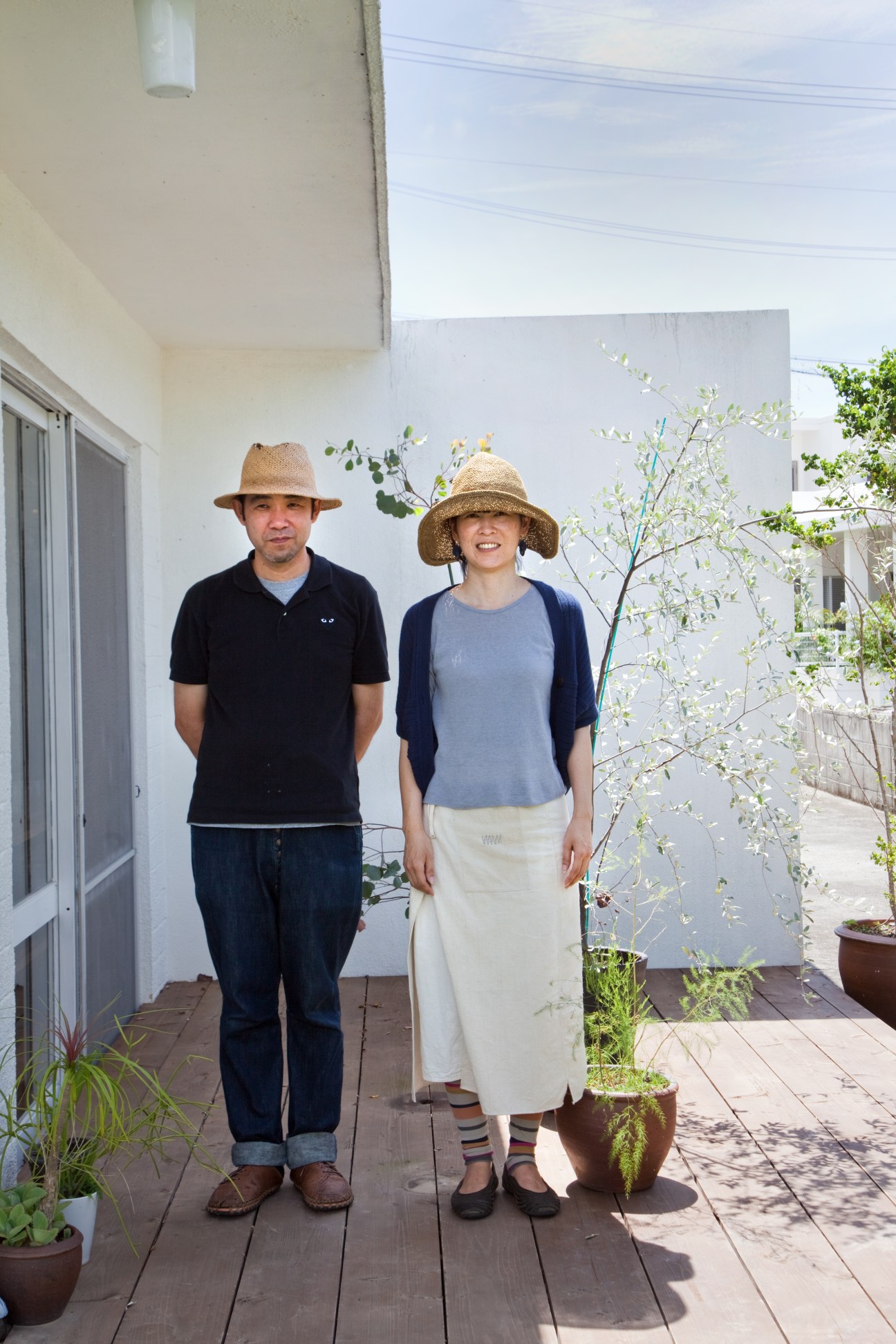 Isao and Sayuri Oshiro stand together on a wooden deck outside their white concrete military house in Okinawa.