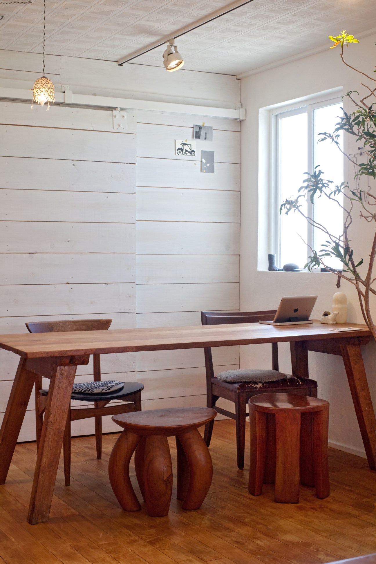 Interior of Ten shop with wooden table, stools, and white shiplap wall featuring pendant lighting.